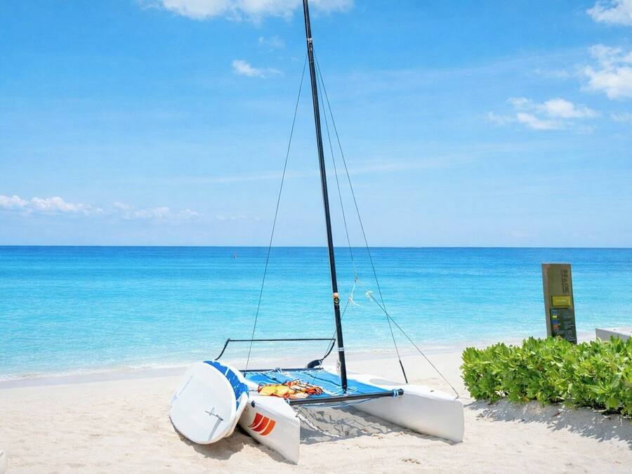 Un velero en una playa arenosa con aguas azules cristalinas y un horizonte lejano.