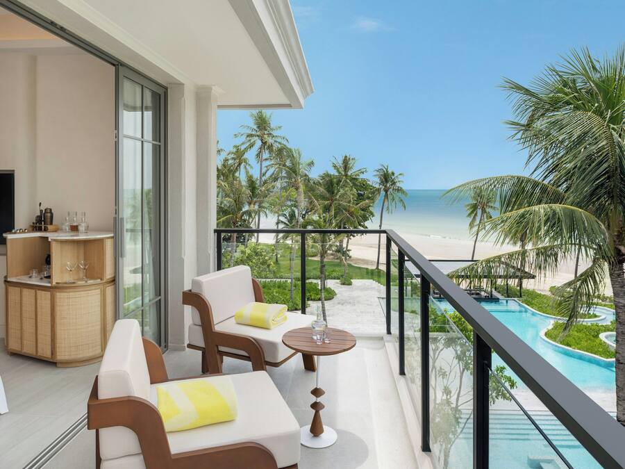 A balcony with a view of the beach and pool, furnished with a sofa, chairs, and a small table.