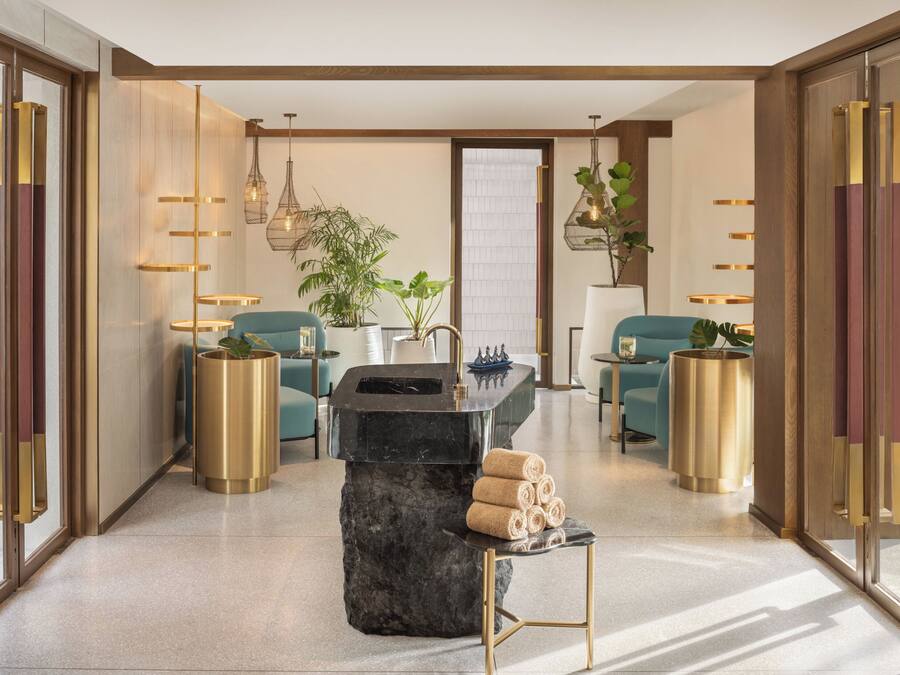 A modern bathroom with a marble sink, gold accents, and a potted plant.
