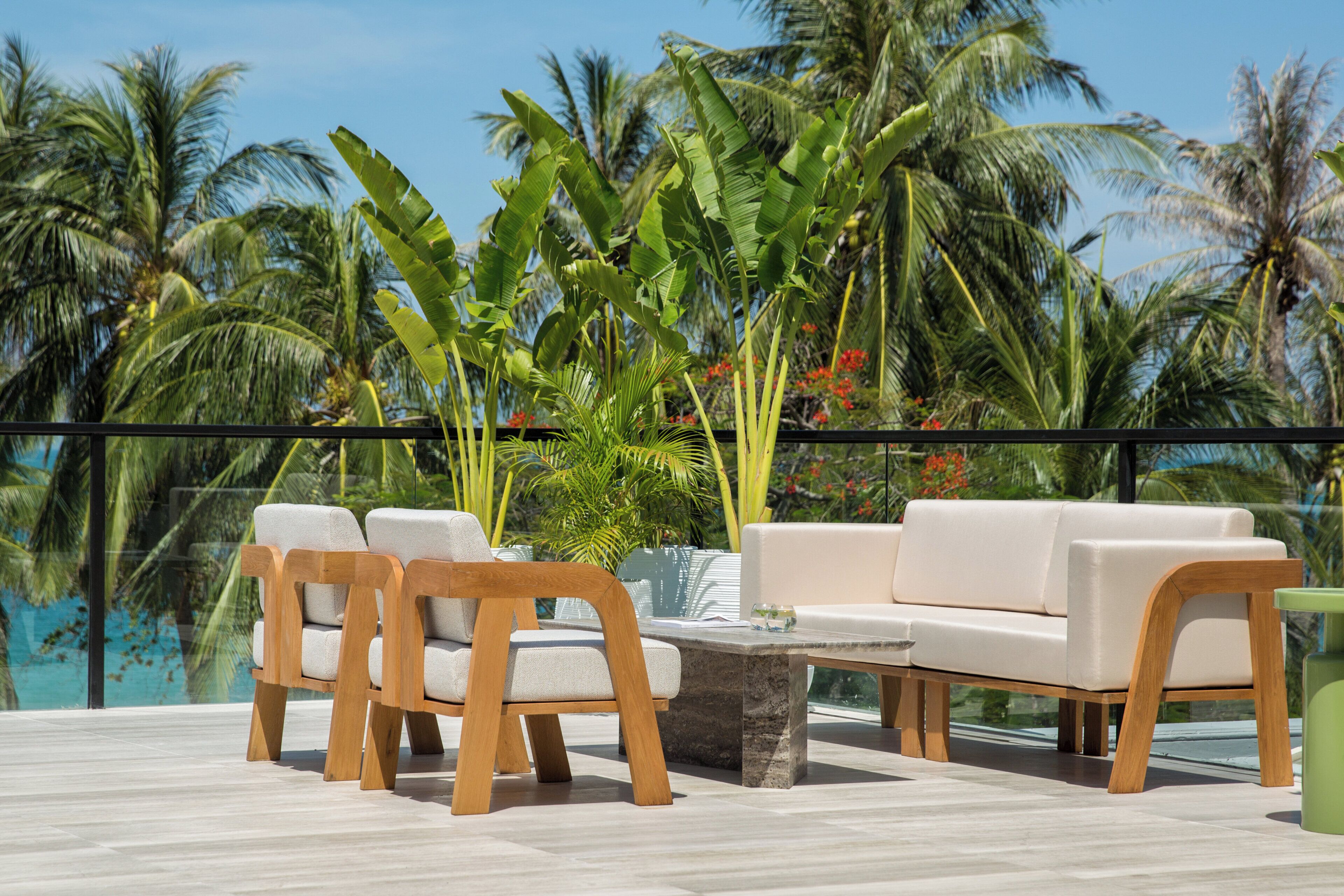 A terrace with a sofa and chairs, a table, and a view of palm trees and a pool.