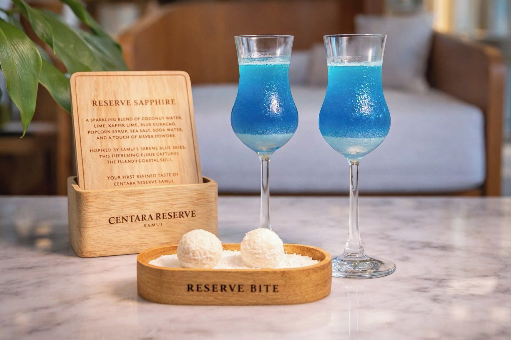 Dos vasos de cóctel azul, una señal de madera con texto y un cuenco de madera con esferas blancas.