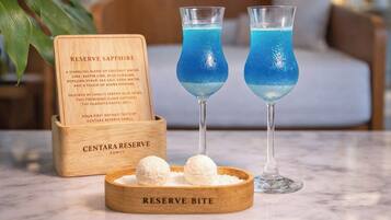 Dos vasos de cóctel azul, una señal de madera con texto y un cuenco de madera con esferas blancas.
