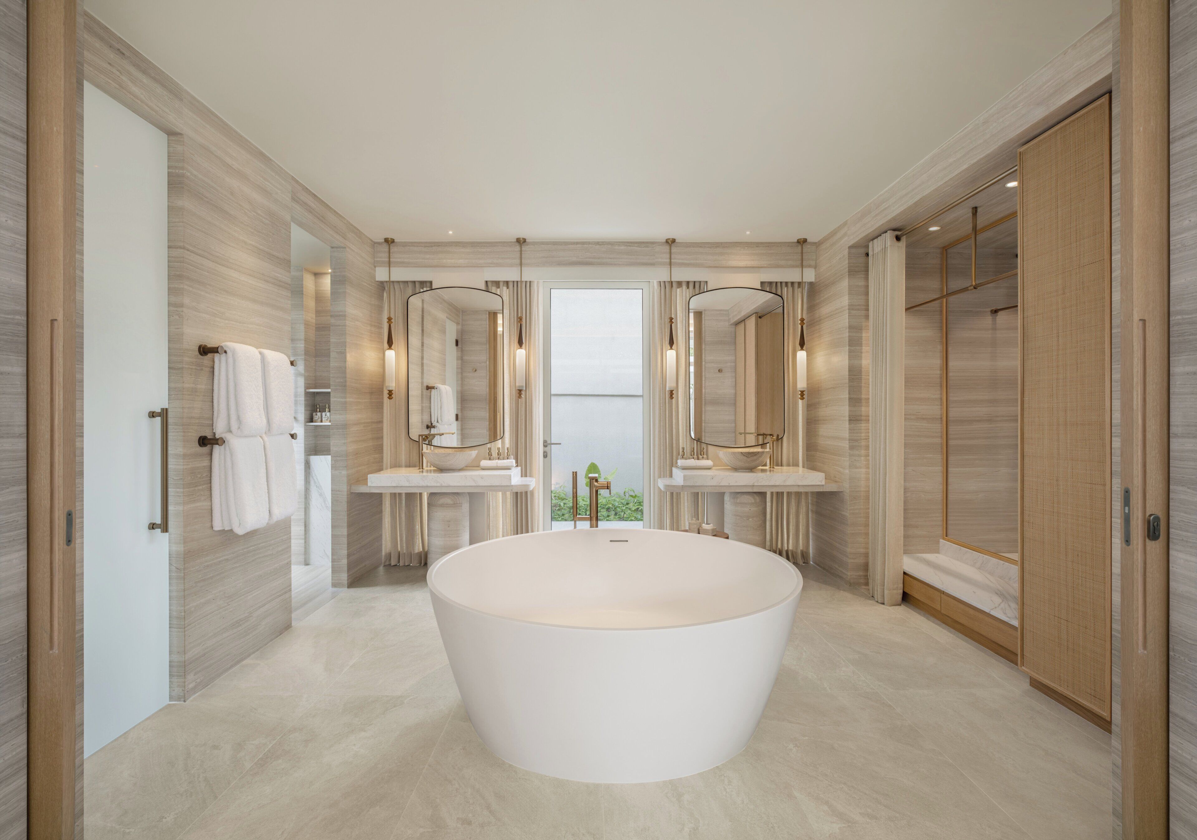 A modern bathroom with a large freestanding bathtub, two vanity mirrors, and a view through the door.