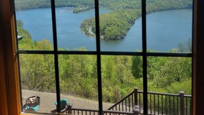 Vista a través de una ventana con diseño de cuadrícula, hacia un lago rodeado de colinas boscosas.