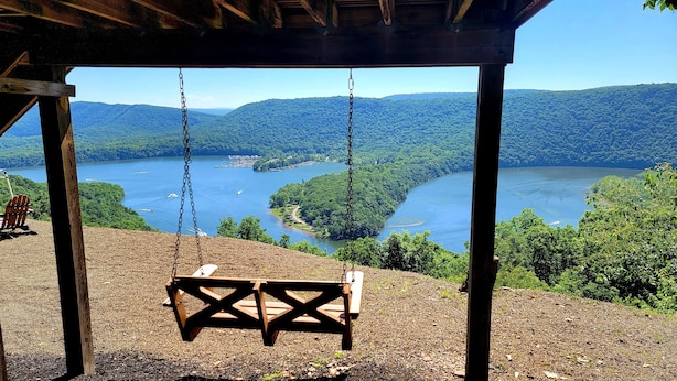 Una silla mecedora de madera bajo una estructura de madera con vista a un lago rodeado de colinas.