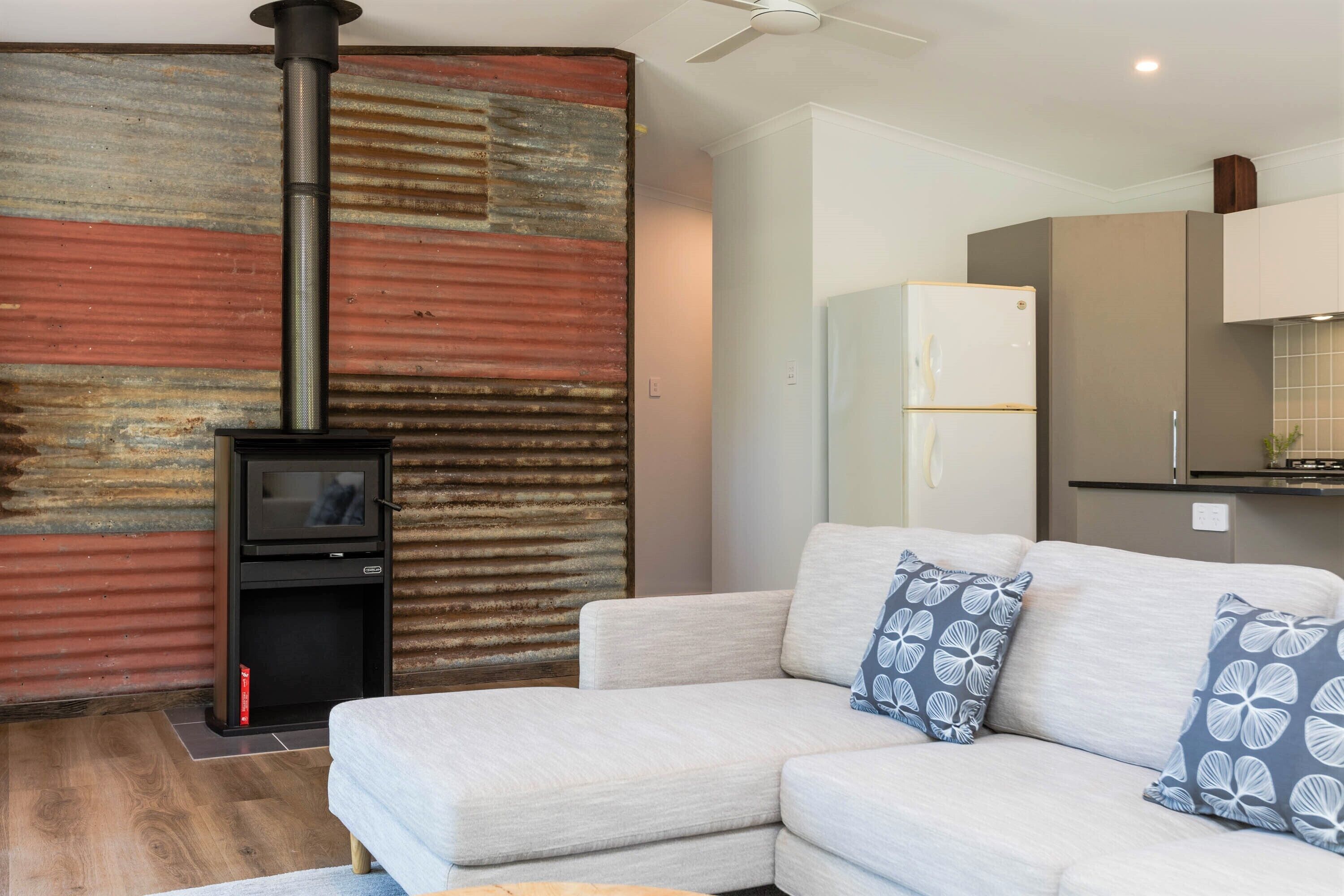 A modern living room with a sofa, decorative pillows, a fireplace, and a kitchen area with cabinets and a refrigerator.