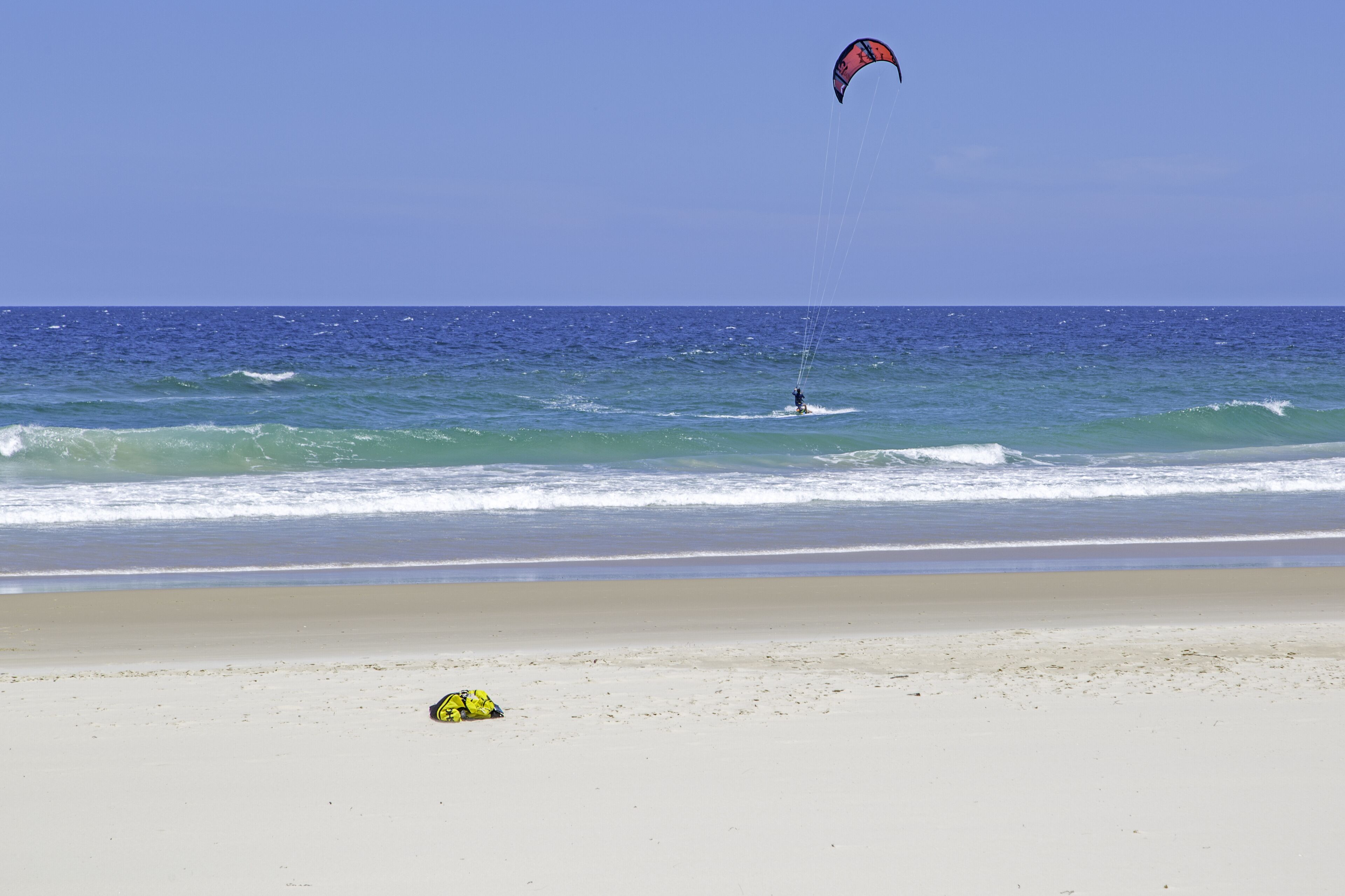 Una playa con una persona parapenteando y un objeto amarillo sobre la arena.