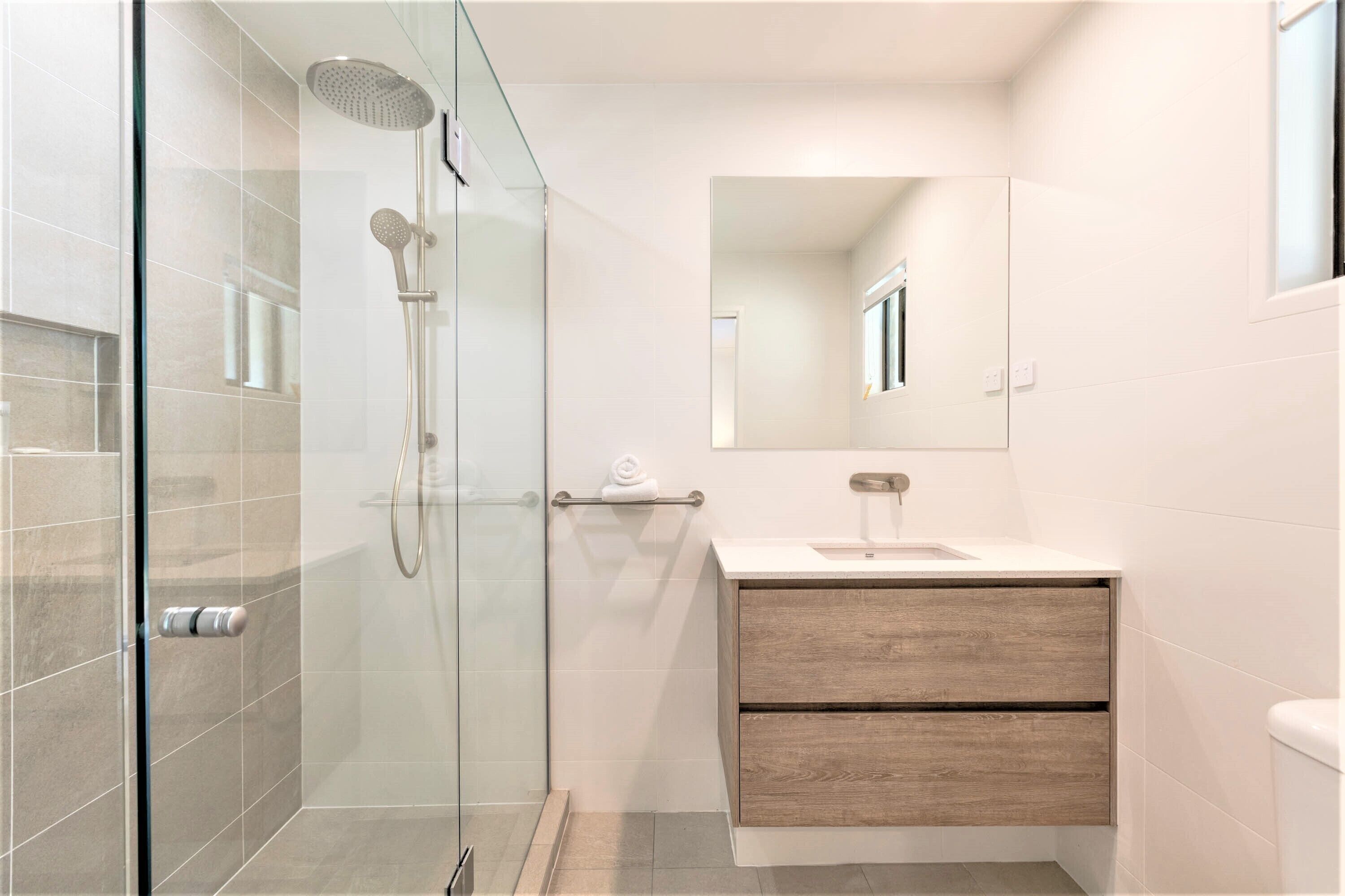 Un baño moderno con ducha envuelta en vidrio, tocador de madera y un espejo grande.