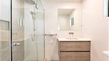 Un baño moderno con ducha envuelta en vidrio, tocador de madera y un espejo grande.