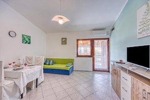 En stue med spisebord, grøn sofa, fjernsyn og et vindue med gardiner.