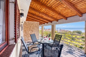 A balcony with a wooden ceiling, a glass table with chairs, and a view of a vineyard and sea. - Turquoise Apartment Sea View, Jasenice, Croatia (Jasenice)