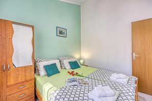 A bedroom with a bed, pillows, a wooden wardrobe, a framed picture on the wall, and a magazine on the bed.