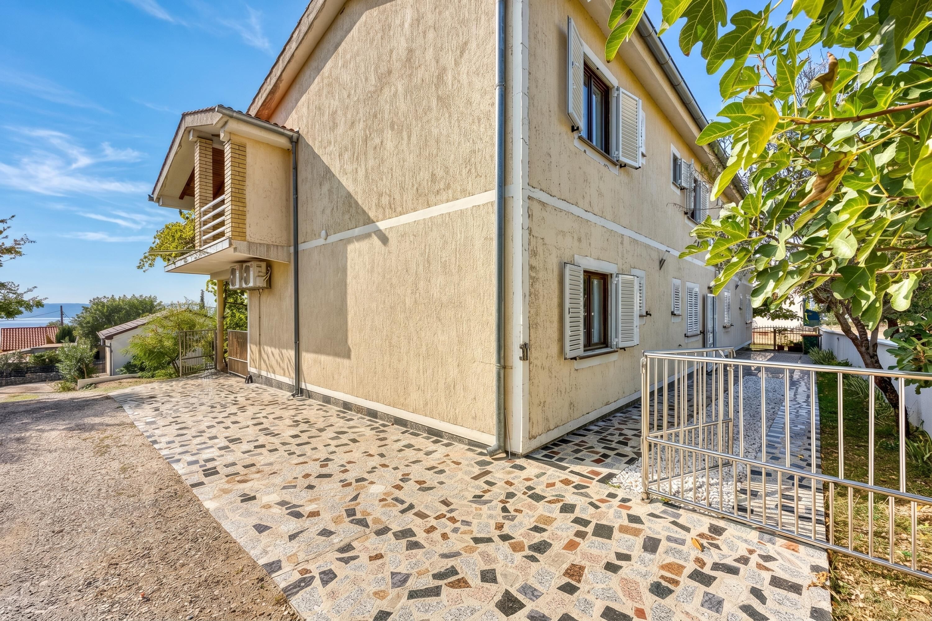 Une maison à deux étages avec une terrasse carrelée, un balcon et un portail en métal.