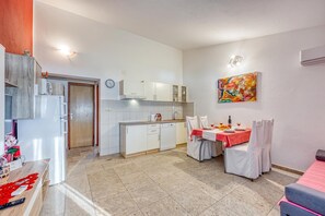 A compact kitchen with white cabinets, a dining area with a table set for two, and a colorful abstract painting on the wall.