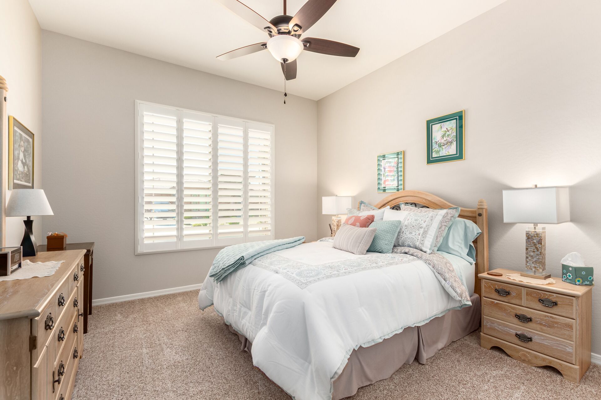 A bedroom with a bed, bedside tables, a dresser, a ceiling fan, and a window with blinds.