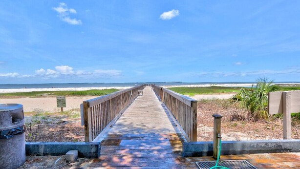 Une promenade en bois menant à une plage, avec un ciel dégagé.