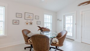 Une pièce avec une table à plateau de verre entourée de chaises en osier, un ventilateur de plafond et des tableaux encadrés accrochés aux murs.