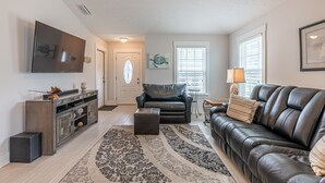 Un salon comprenant un canapé en cuir noir, un fauteuil en cuir noir, un meuble de rangement en bois et un tapis à motifs.