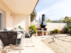 Een terras buiten met een tafel, stoelen, een barbecue en planten in potten.