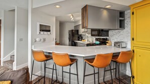 Una cocina moderna con una isla central, taburetes de bar y un armario amarillo.