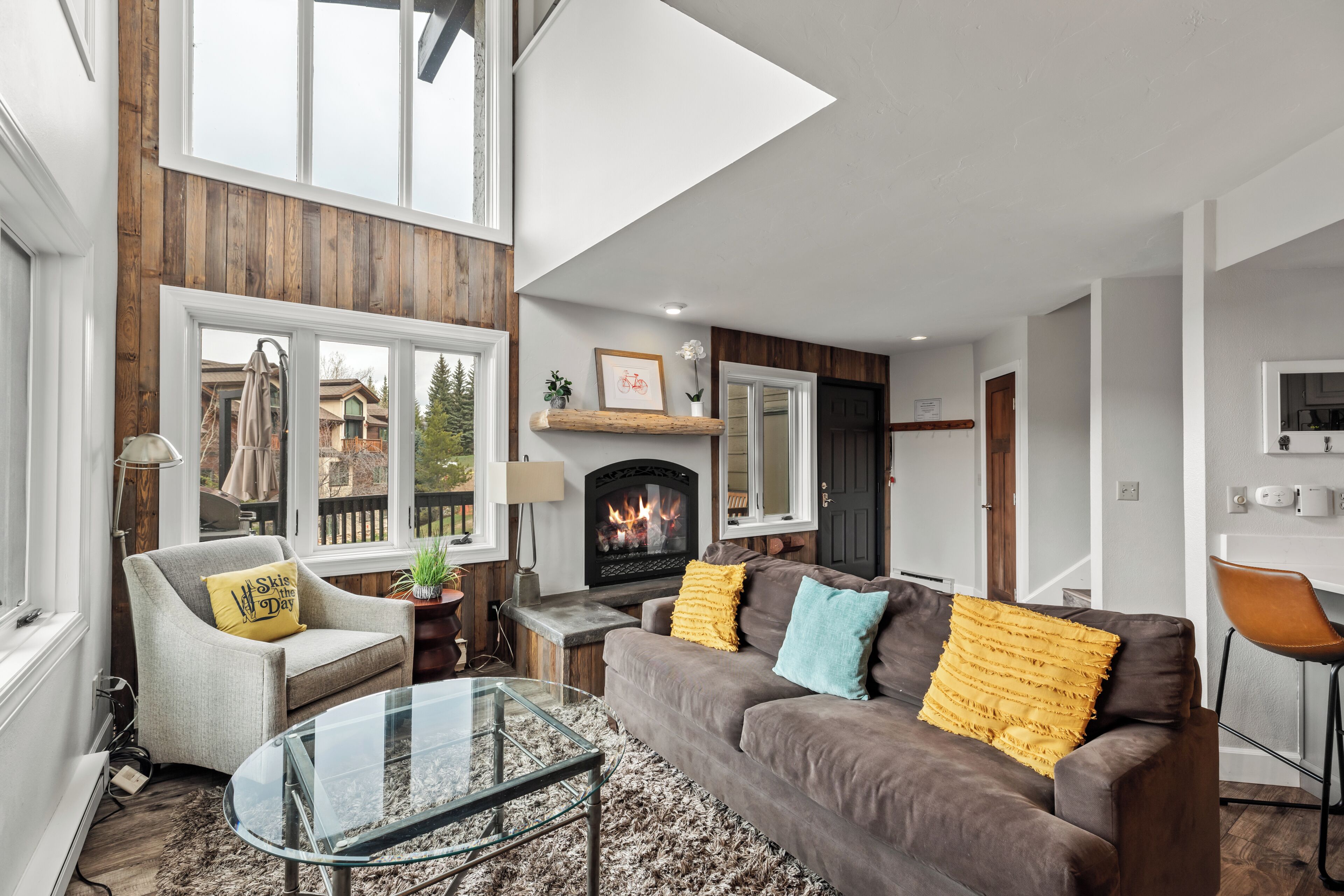 A modern living room with a fireplace, a glass coffee table, and a sofa with decorative pillows.