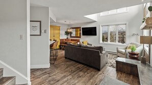 Un salón espacioso con un sofá de color oscuro, una mesa de centro de madera y un comedor con armarios amarillos y una mesa de madera.