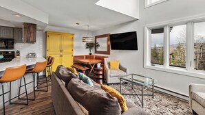 Una cocina moderna con armarios amarillos, un comedor con mesa de madera, y una sala de estar con sofá y sillones.