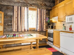 A rustic kitchen with wooden cabinets, a wooden table, and a window with striped curtains. - Luostonseita 1 by Interhome (Sodankylä)