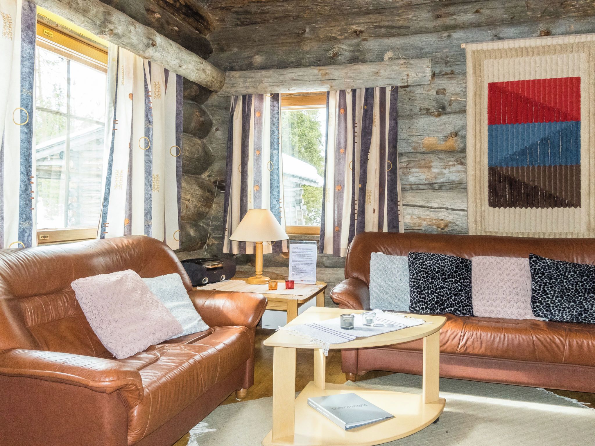A cozy log cabin interior with leather sofas, a wooden coffee table, and a lamp.