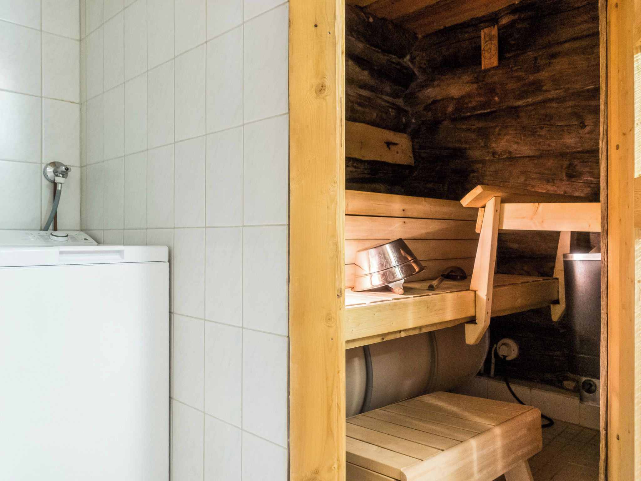 A bathroom with a white tiled wall, a wooden bench, and a sink with a faucet.