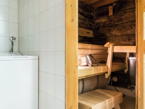 Une salle de bain avec un mur recouvert de carreaux blancs, un banc en bois et un lavabo avec un robinet.