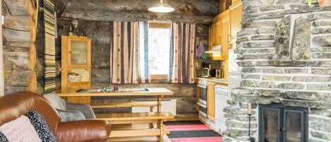 A cozy cabin interior with a stone fireplace, wooden furniture, and a kitchen area.