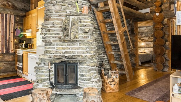 Een rustiek interieur met een stenen openhaard, houten balken en een gezellige zithoek.