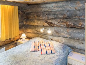 A log cabin-style room with a bed, a nightstand with a lamp, and a window with yellow curtains. - Luostonseita 1 by Interhome (Sodankylä)