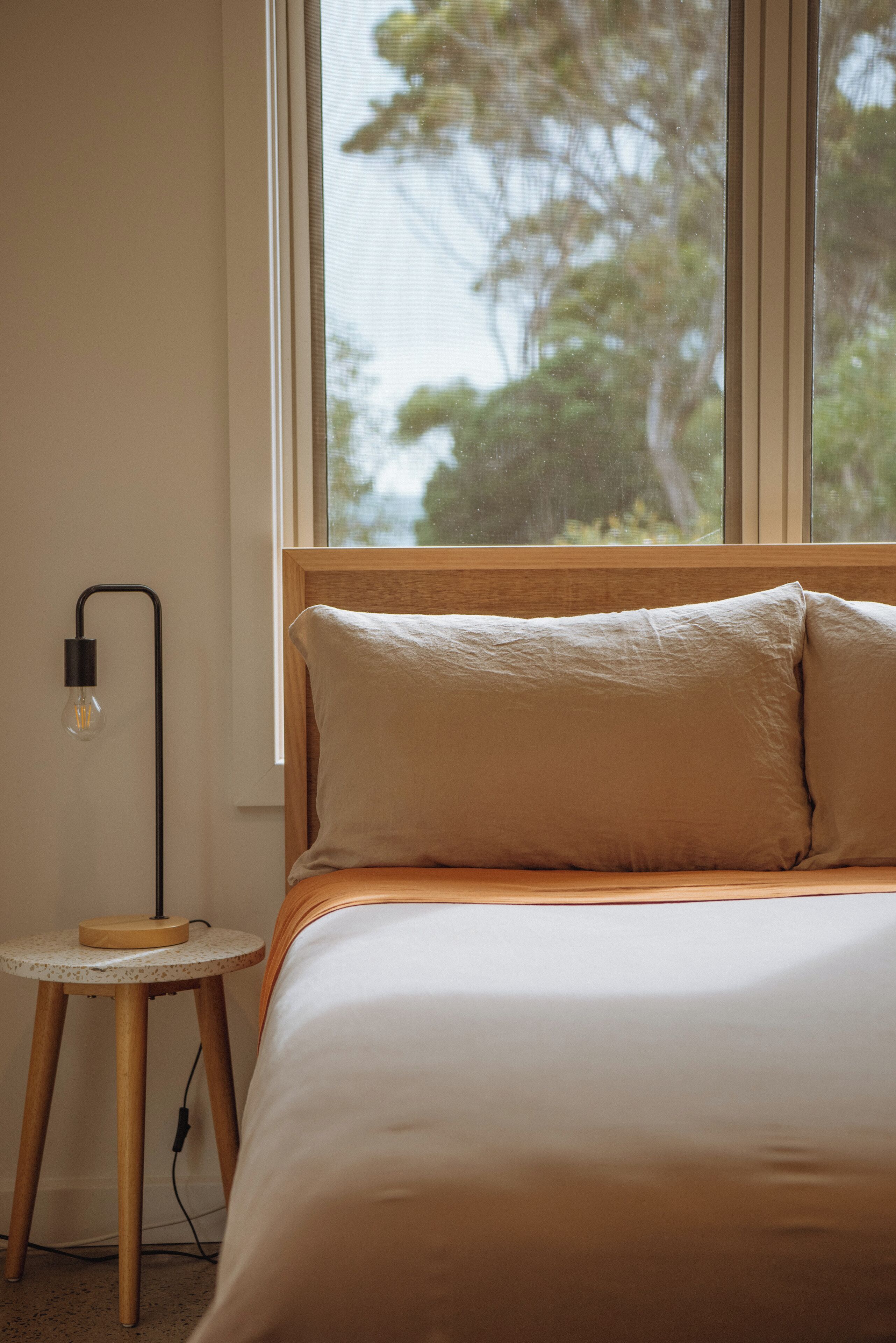 Une chambre à coucher avec un lit, une fenêtre et une petite table avec une lampe.
