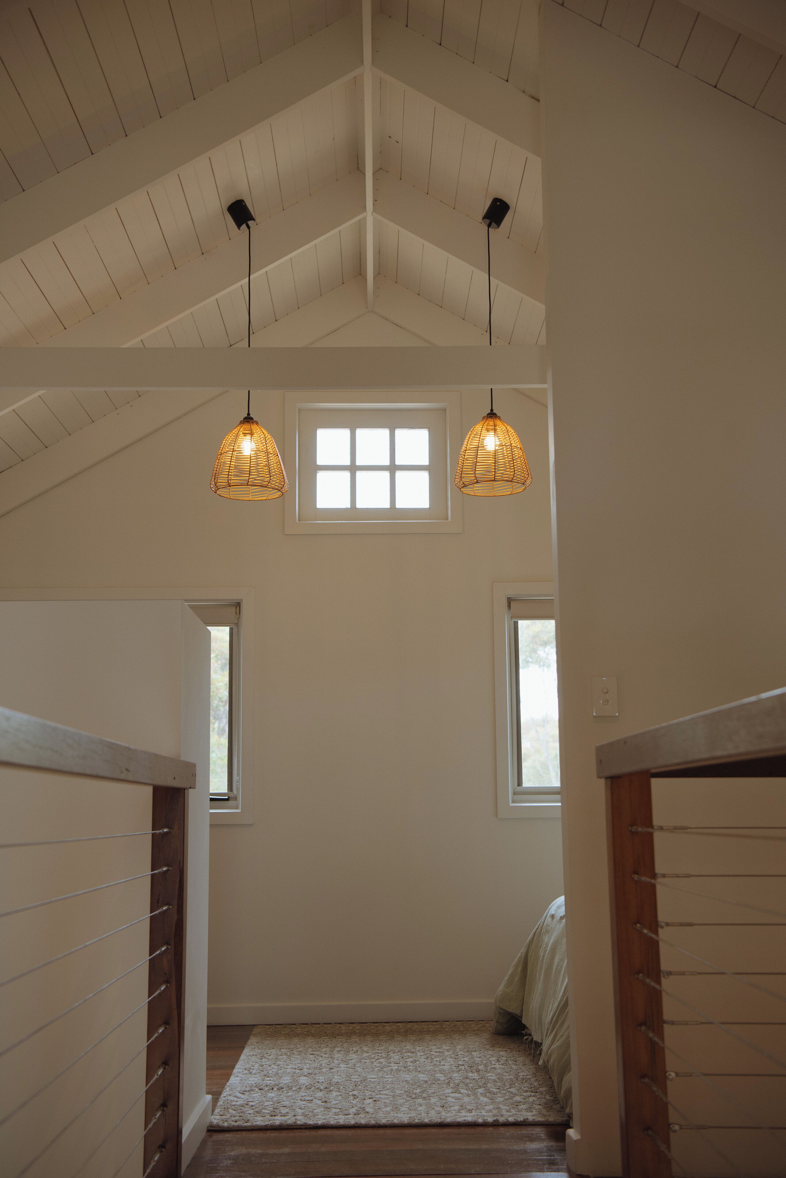 A room with a sloped ceiling, two hanging pendant lights, a window, and a wooden floor.