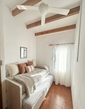 Un dormitorio con cama, ventilador de techo, vigas de madera, ventana con cortinas e interruptor de luz en la pared.