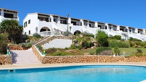 Une piscine bordée d’un mur en pierre et dotée d’un escalier menant à un bâtiment blanc orné d’arcades et d’un balcon.