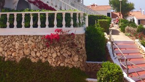 Un bâtiment avec une base en pierre, des balustrades de balcon blanches et des fleurs rouges.