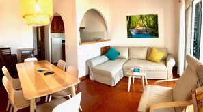 Una sala de estar con un sofá, una mesa de comedor, sillas, un taburete pequeño y un cuadro en la pared.