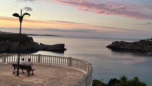Un banc où sont assis deux personnes, une étendue d’eau calme et une côte rocheuse.
