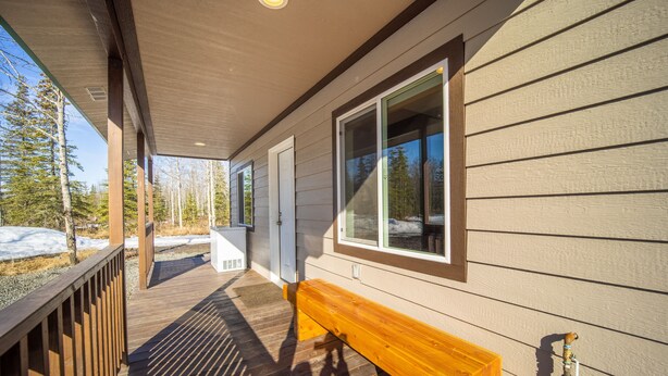A wooden deck with a bench, a covered porch, and a window with a view of trees and snow.