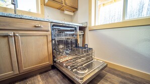 A kitchen with wooden cabinets, a built-in dishwasher, and a window with a view of trees.