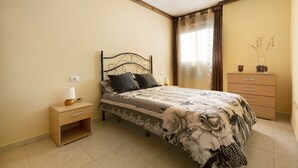 A bedroom with a bed, nightstand, dresser, and a window with curtains. - Vacation Home "Apartamento Vistas de Icod" with Mountain View, Sea View & WiFi (Icod de los Vinos)