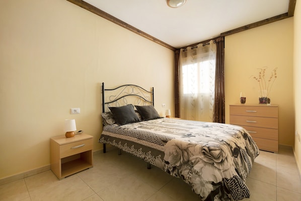 A bedroom with a bed, nightstand, dresser, and a window with curtains.