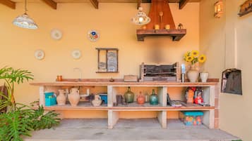 A kitchen with shelves holding various kitchenware, a hanging light fixture, and a wall-mounted shelf with decorative items.
