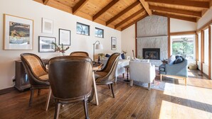 Amplia sala de estar con suelo de madera, chimenea y zona de comedor con sillas de cuero.