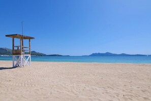 Una playa con una torre de salvavidas, cielo azul despejado y montañas a lo lejos.