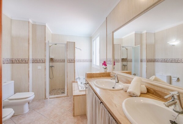 Un baño con ducha, dos lavamanos, inodoro y un espejo grande.