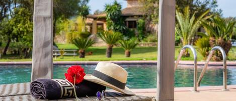 Un área de descanso junto a la piscina con un sombrero, gafas de sol y una toalla.